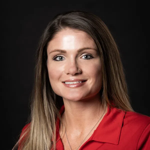Woman with long blonde hair wearing a red shirt with a construction company logo on black background.