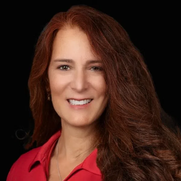 Smiling woman with long red hair wearing a red polo shirt with a construction company logo on black background