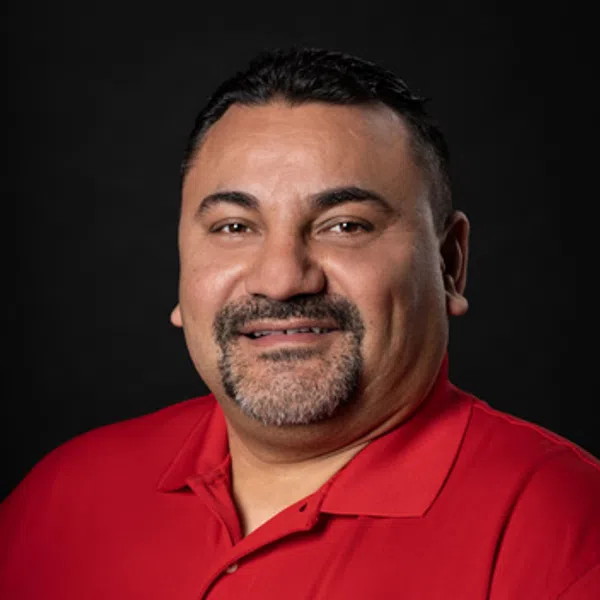 Man wearing a red polo shirt with a circular company logo, smiling against a black background.