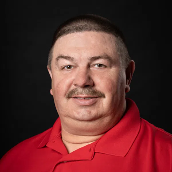 Man with short hair and mustache wearing red polo shirt with a circular company logo on black background