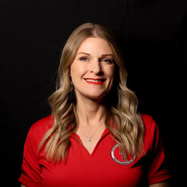 Smiling woman with long blonde hair wearing a red polo shirt with a logo on black background