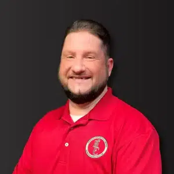 Smiling man with dark beard wearing red polo shirt with logo against black background