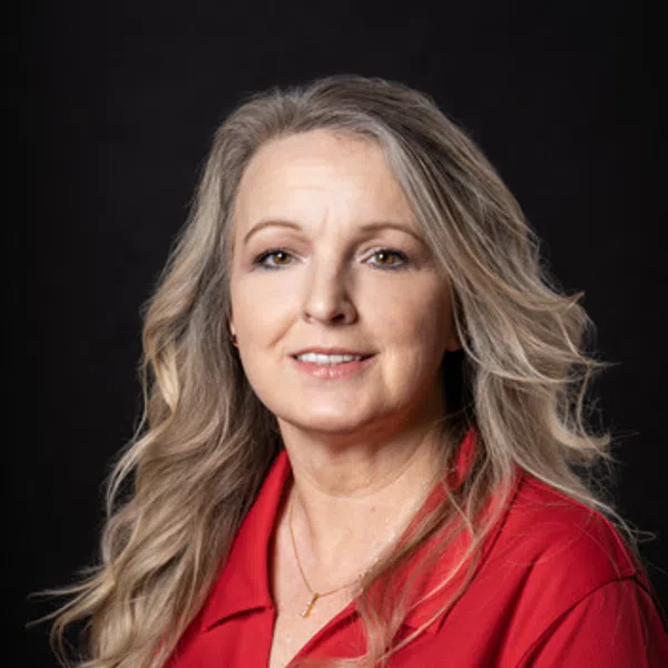 Portrait of a smiling woman with long blonde hair wearing a red polo with an embroidered logo on black background