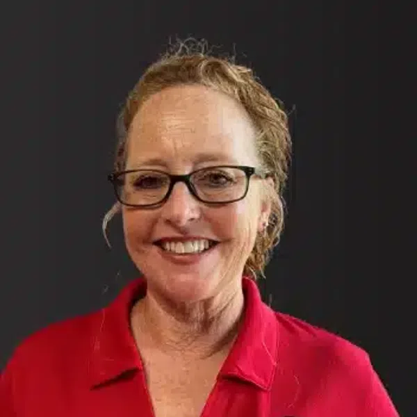 Smiling woman with glasses wearing a red polo shirt with a round logo on the chest against a black background