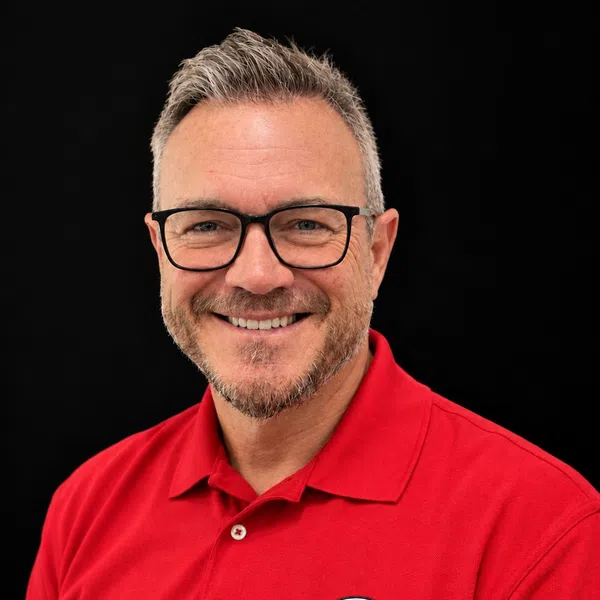 Man with glasses smiling wearing a red polo shirt with Harrison Contracting Company logo against black background