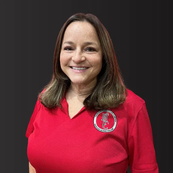 Smiling woman with shoulder-length brown hair wearing a red polo shirt with a logo on black background