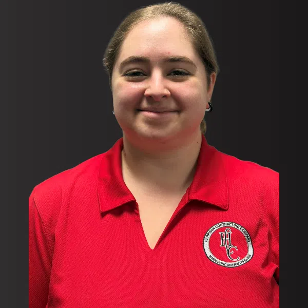 Smiling woman wearing a red polo shirt with a Harrison Contracting Company logo on a black background