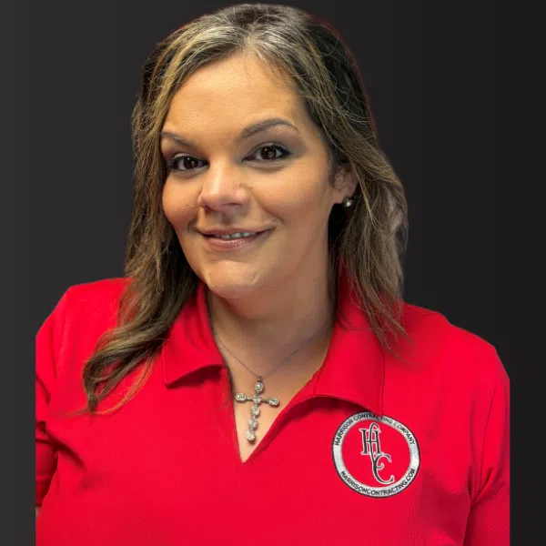 Smiling woman wearing a red polo with cross necklace and company logo on dark background
