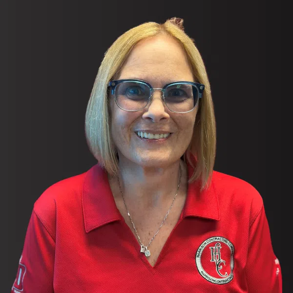 Smiling woman with blonde hair and glasses wearing a red polo shirt with a Harrison Contracting logo.