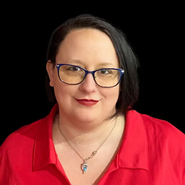 Woman with glasses wearing a red shirt with a logo on a black background smiling gently.