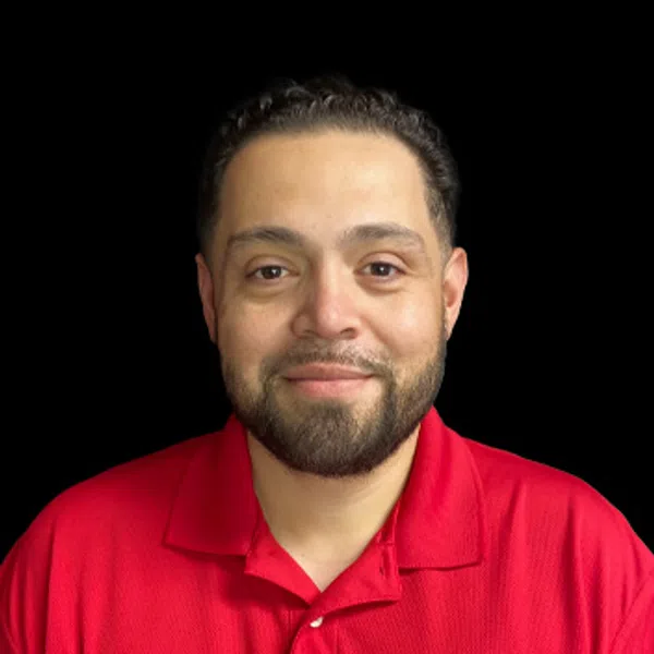 Smiling man with short dark hair and beard wearing red polo shirt with a company logo on black background.