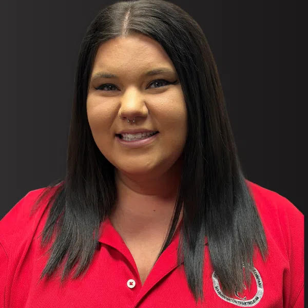 Smiling woman with long black hair in a red collared shirt with septum piercing against dark background