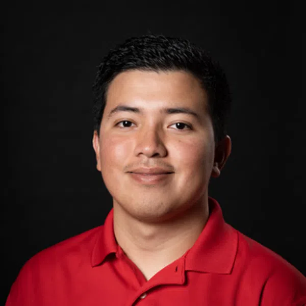 Man wearing red polo shirt with a logo smiles against a black background in a professional portrait.