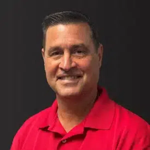 Smiling man wearing a red polo shirt with an embroidered circular logo on a black background