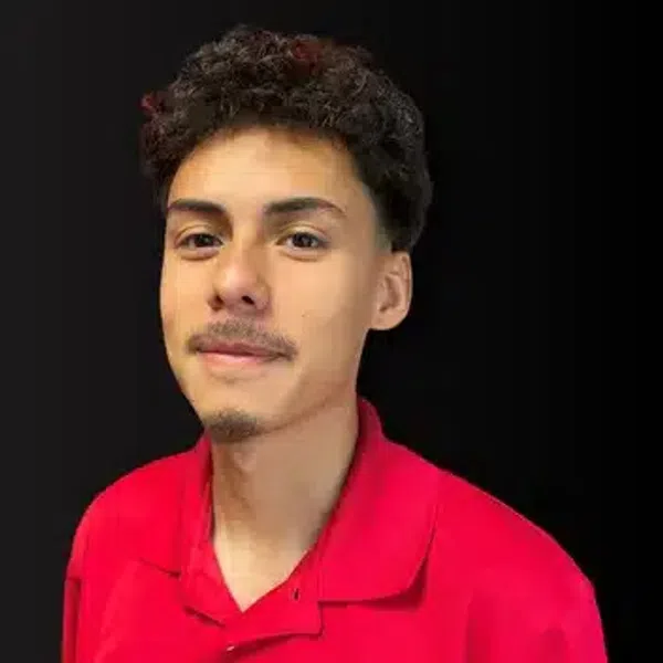 Young man with curly hair wearing a red polo shirt with an embroidered logo against a black background