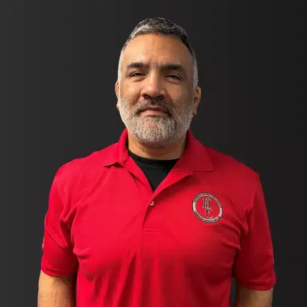 Middle-aged man with gray beard wearing a red polo shirt with a circular logo on black background