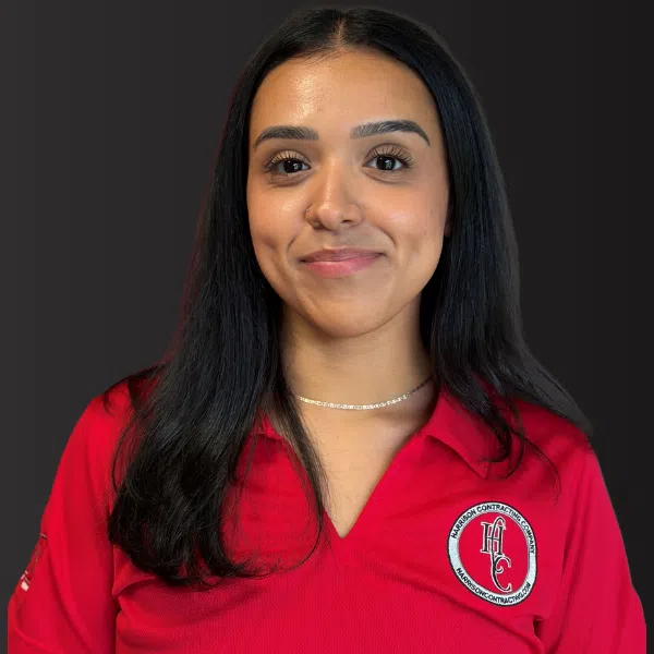Young woman with long black hair wearing a red polo shirt with a Harrison Contractors logo on a dark background