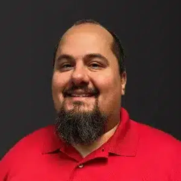 Smiling man with beard wearing a red polo shirt with a circular embroidered logo on a black background