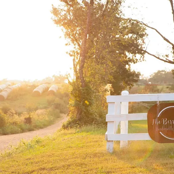 Sunny rural farm entrance with white fence and sign for The Berry Farm in Bentonville Arkansas