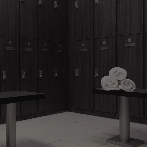 Modern locker room with dark wood lockers, benches, and rolled white towels on one bench.