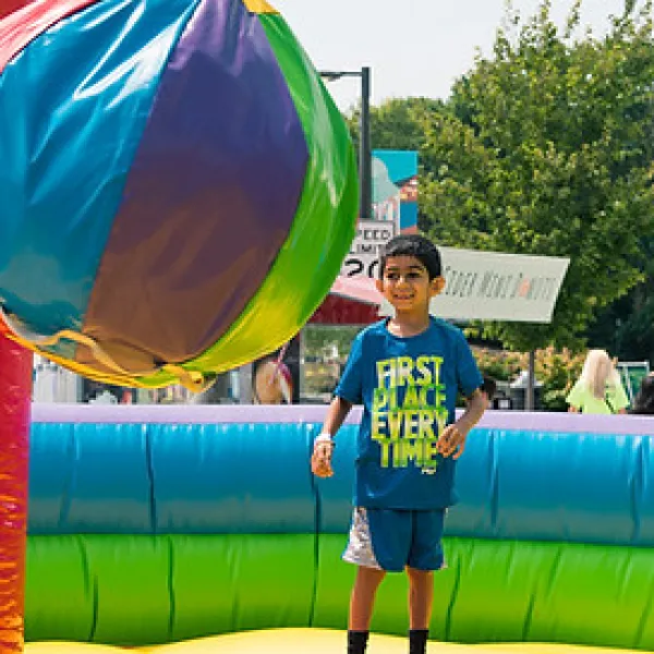 Children playing with a large colorful inflatable ball in an outdoor bounce house on a sunny day.