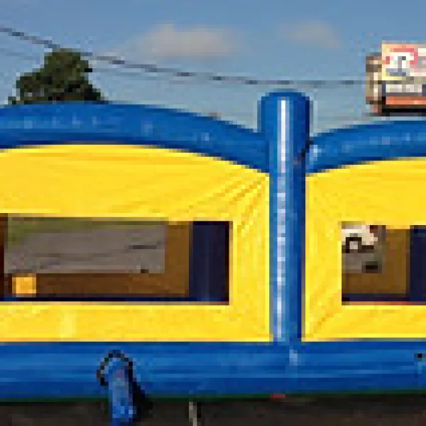 Blue and yellow inflatable bounce house with windows set up outdoors on pavement under blue sky.