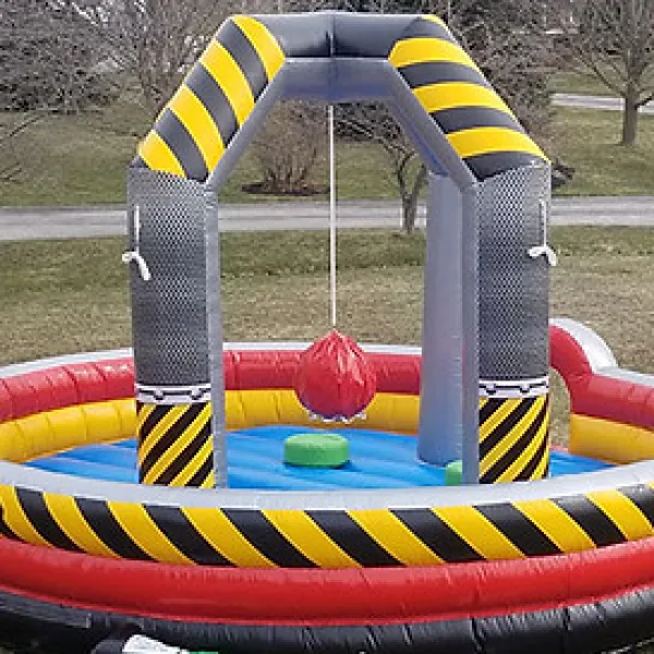 Colorful inflatable wipeout game with black and yellow arch, red swinging ball, and round platform outdoors on grass.