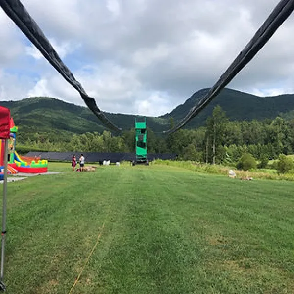 Zipline cables stretching over green grassy field with mountains and cloudy sky in background