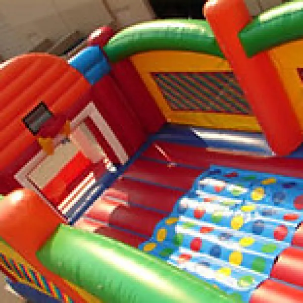 Colorful inflatable bounce house with basketball hoop and polka dot climbing wall outdoors.
