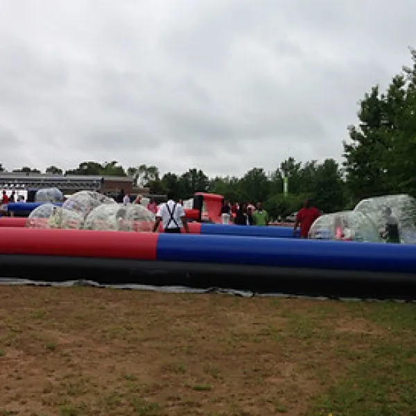 Outdoor human bubble soccer game with inflatable red and blue field and players inside transparent bubbles on a cloudy day