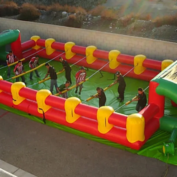 Large inflatable human foosball game with players holding rods inside a red, yellow, and green arena outdoors.