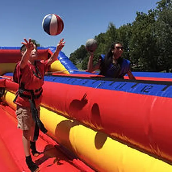 Kids playing on a colorful inflatable obstacle course outdoors on a sunny day with balls in hand.