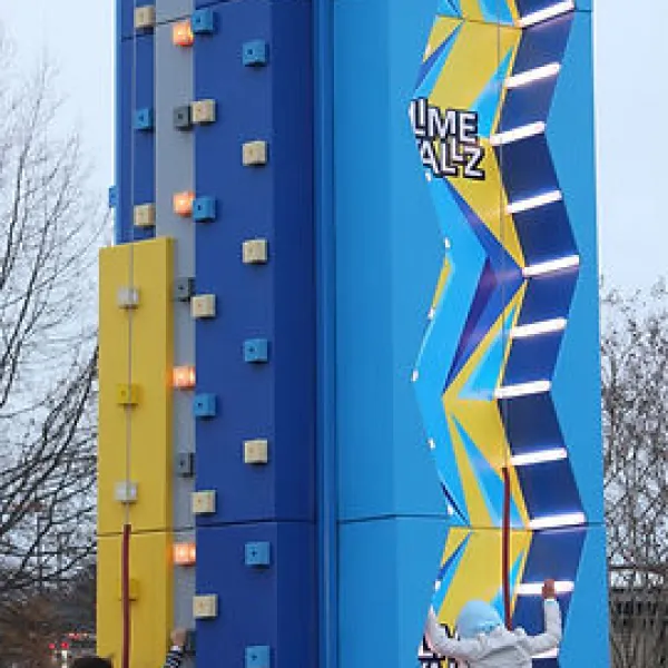 Children climbing colorful interactive outdoor rock climbing walls with spectators watching on a clear day.