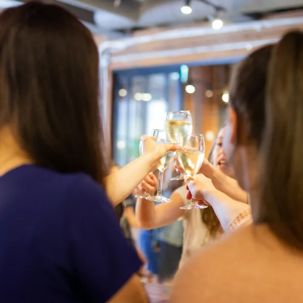 Group of women raising glasses of white wine in a cheerful toast at an indoor gathering.