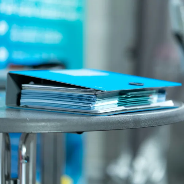 Thick blue binder filled with documents resting on a round metal table in a blurred office environment.