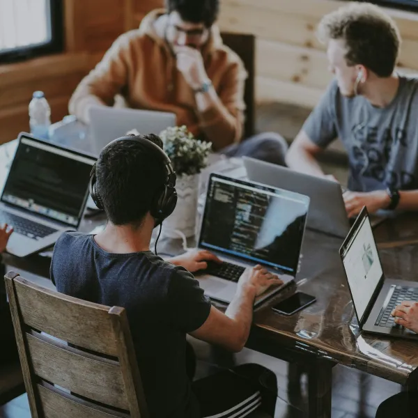 Group of young professionals collaborating on laptops around a wooden table in a casual office setting
