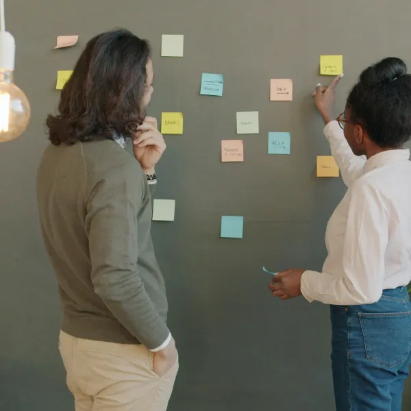 Two coworkers brainstorming with colorful sticky notes on a gray wall in a modern office space