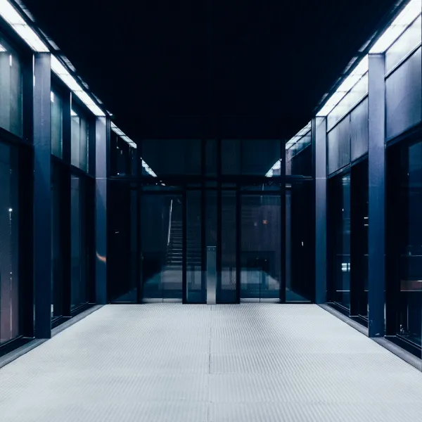 Modern glass-walled corridor with metal framework and bright white floor under cool lighting at night.