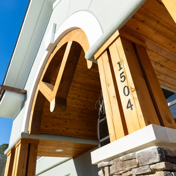 Close-up of a modern house entrance with wooden beams, stone base, and address number 1504 on the pillar.