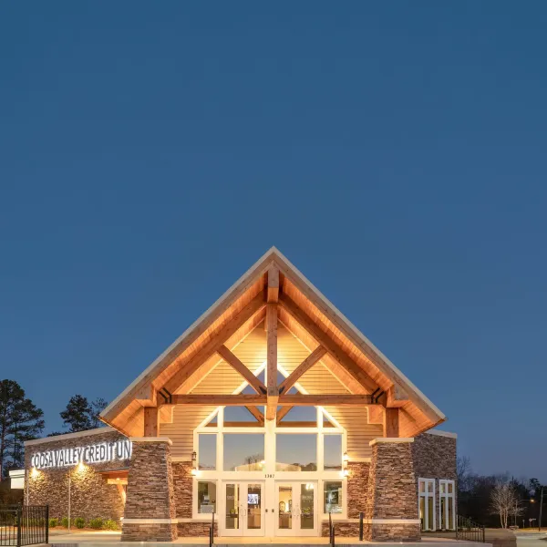 Coosa Valley Credit Union building with stone pillars and large glass windows lit up at dusk under a clear blue sky