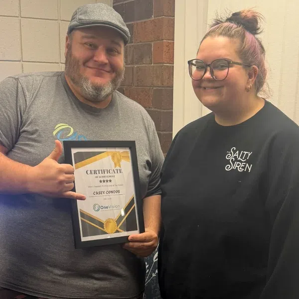 Man holding certificate of achievement while woman stands smiling indoors by brick wall and curtain