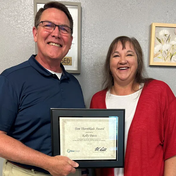 Smiling man and woman holding framed Tom Thornblade Award certificate indoors with framed artwork on wall