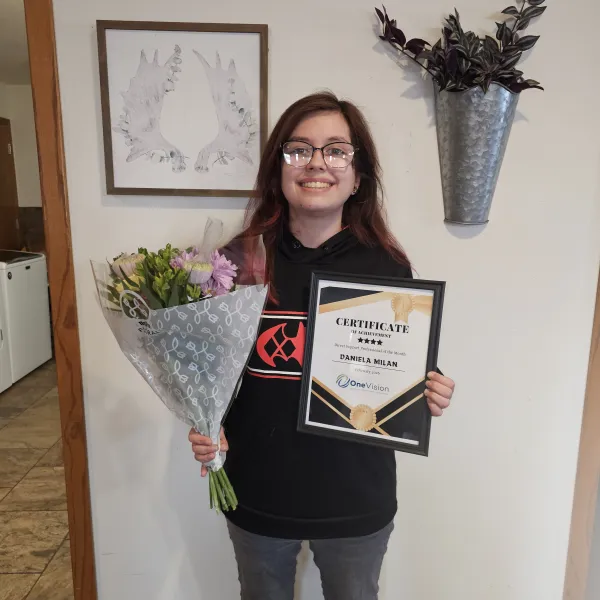 Two smiling women holding framed certificates and bouquets of flowers during an award celebration indoors.