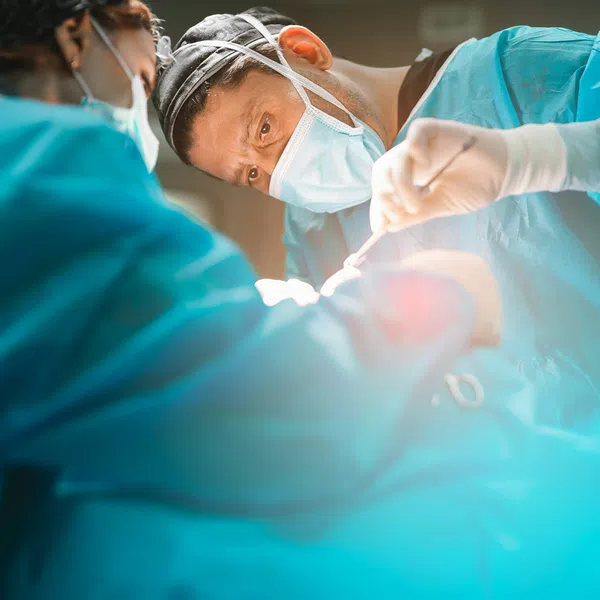 Surgeons wearing masks and scrubs performing a focused surgical operation in a bright operating room.