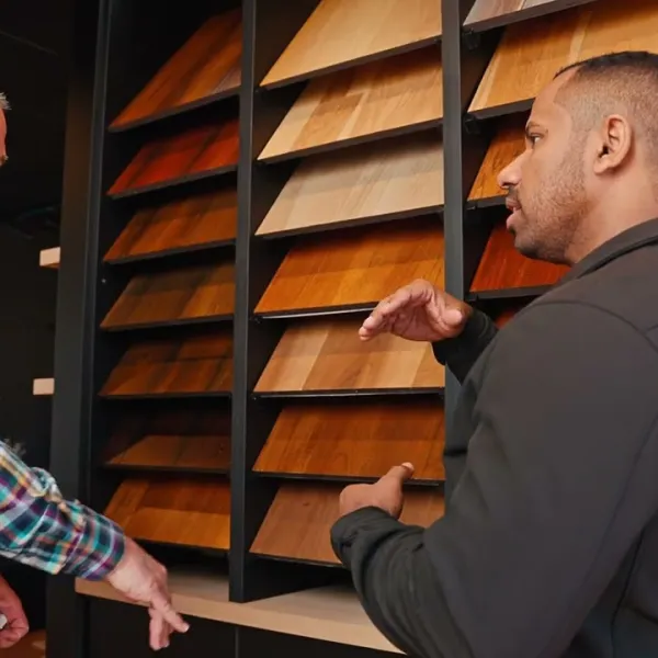 Two men discussing various wood flooring samples displayed on shelves in a showroom.