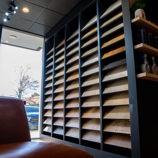 Interior showing wood sample display rack, leather chair, large window, and shelves with decor in a showroom.
