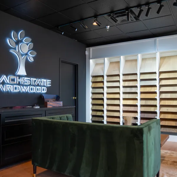 Showroom with hardwood samples displayed on white racks and illuminated Peachstate Hardwood logo on black wall