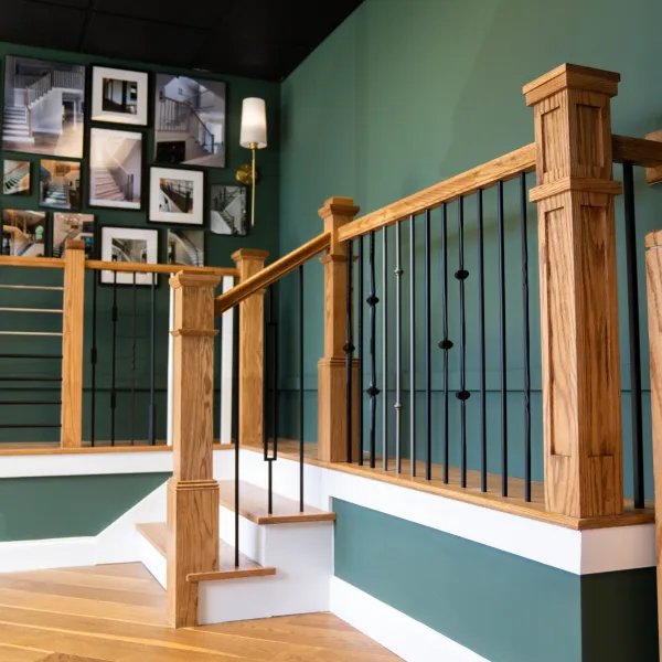 Detailed wooden stair railing with black metal spindles against green walls and framed staircase photos.
