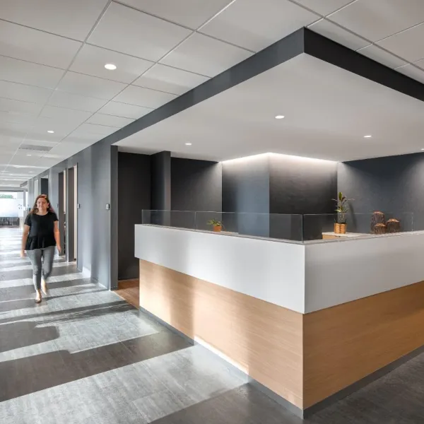 Modern office hallway with natural light, a reception desk, and a woman walking down the corridor.