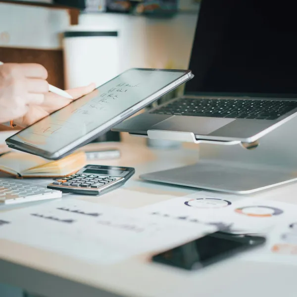 a hand holding a pen over a table with papers and a laptop